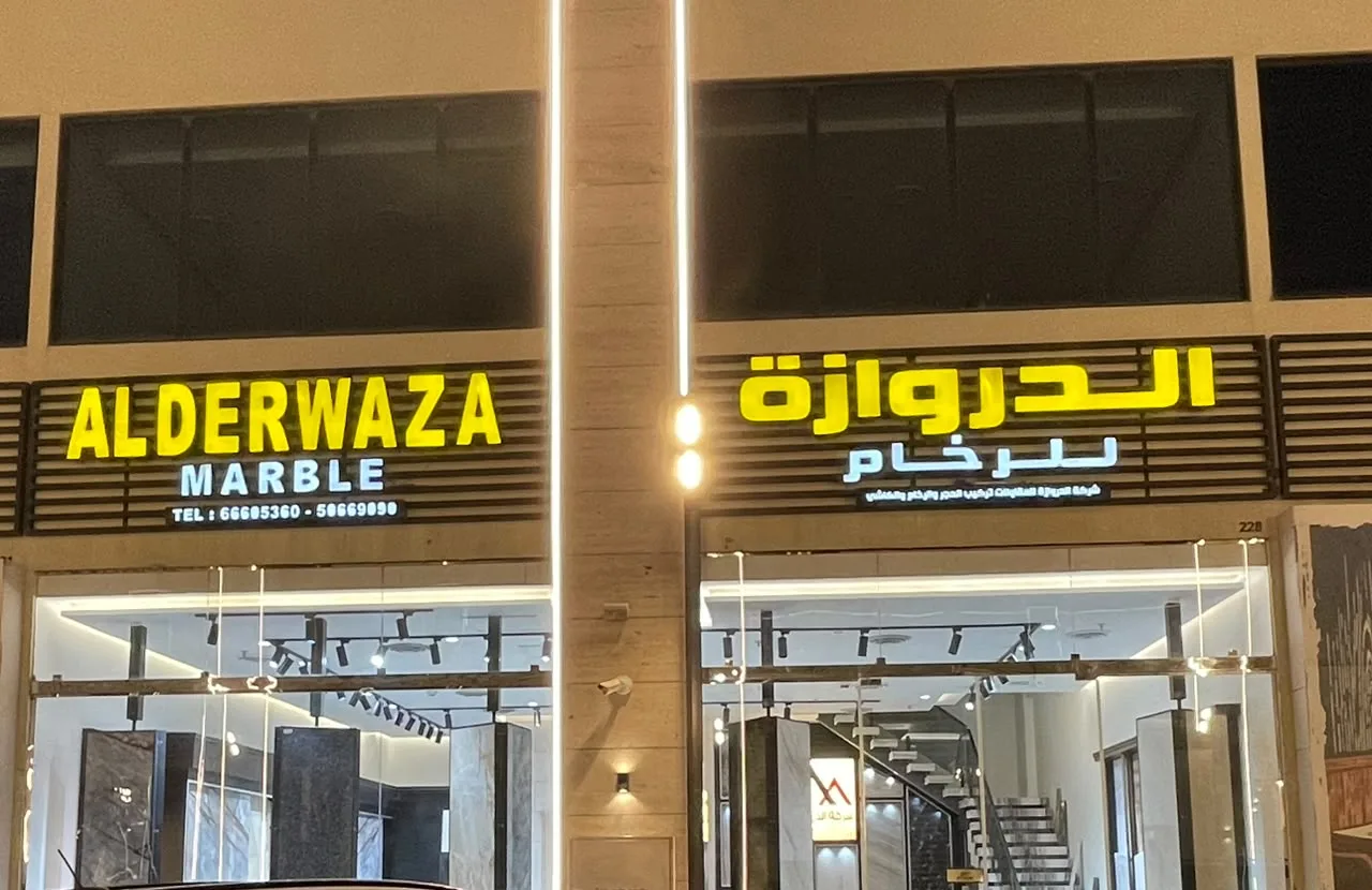 The Alderwaza Marble showroom front at night, with its lit English and Arabic signs and door No. 228