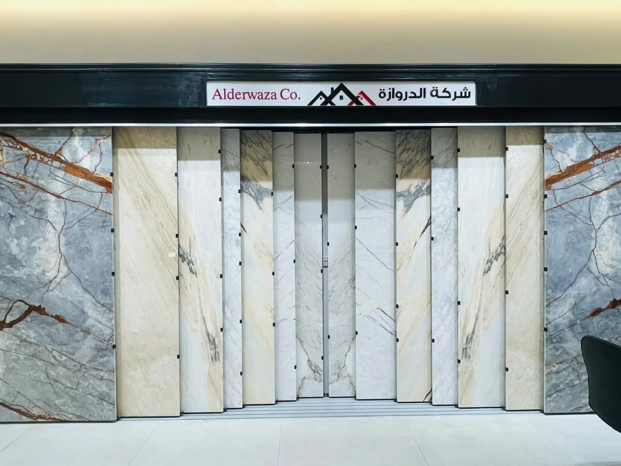 Sliding wall of marble slabs in the Alderwaza showroom, set in mirrored pairs under the Alderwaza Co. sign